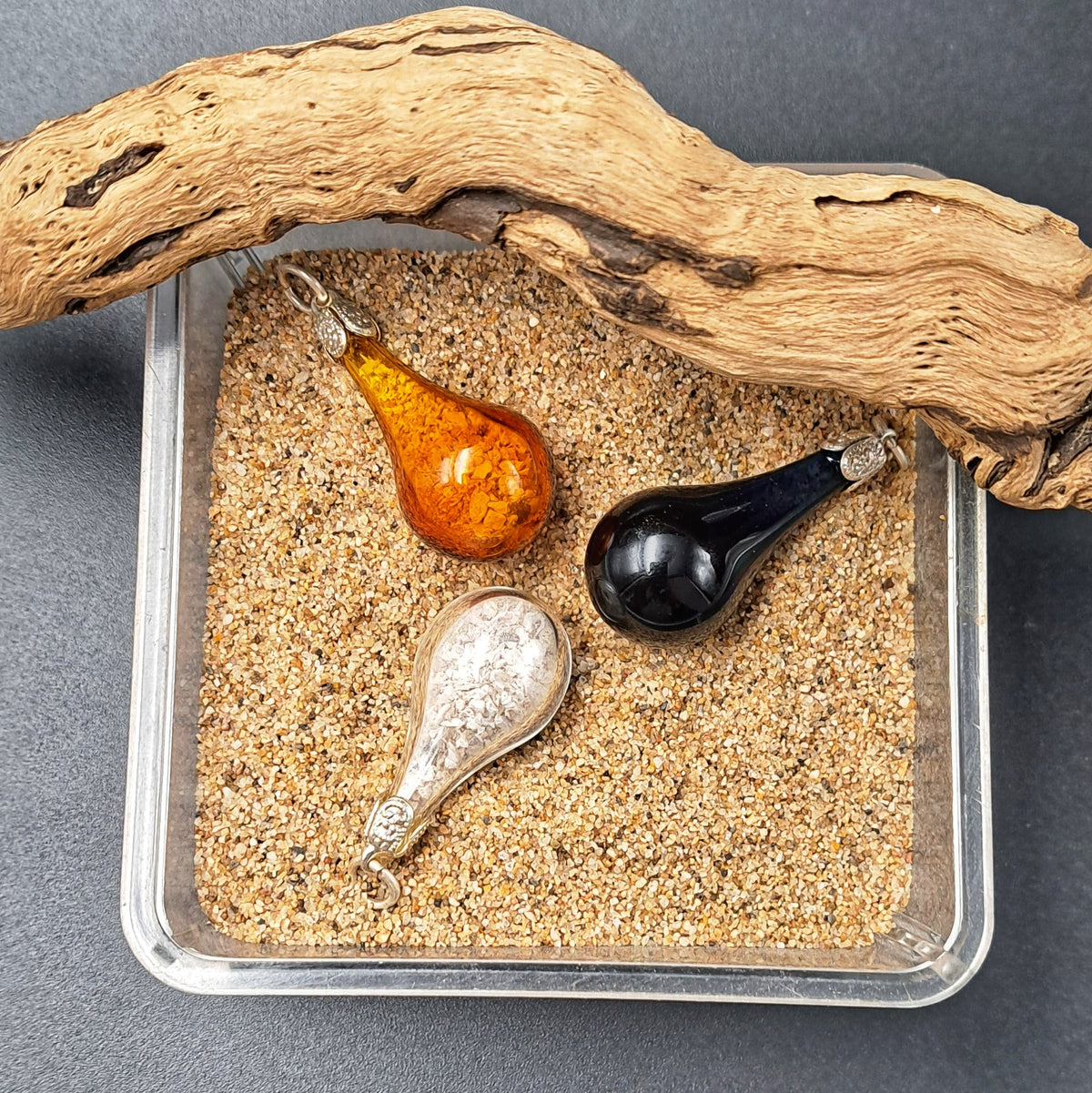 Trois bijoux souvenir en verre posés sur du sable, pour un souvenir de lieu ou de voyage
