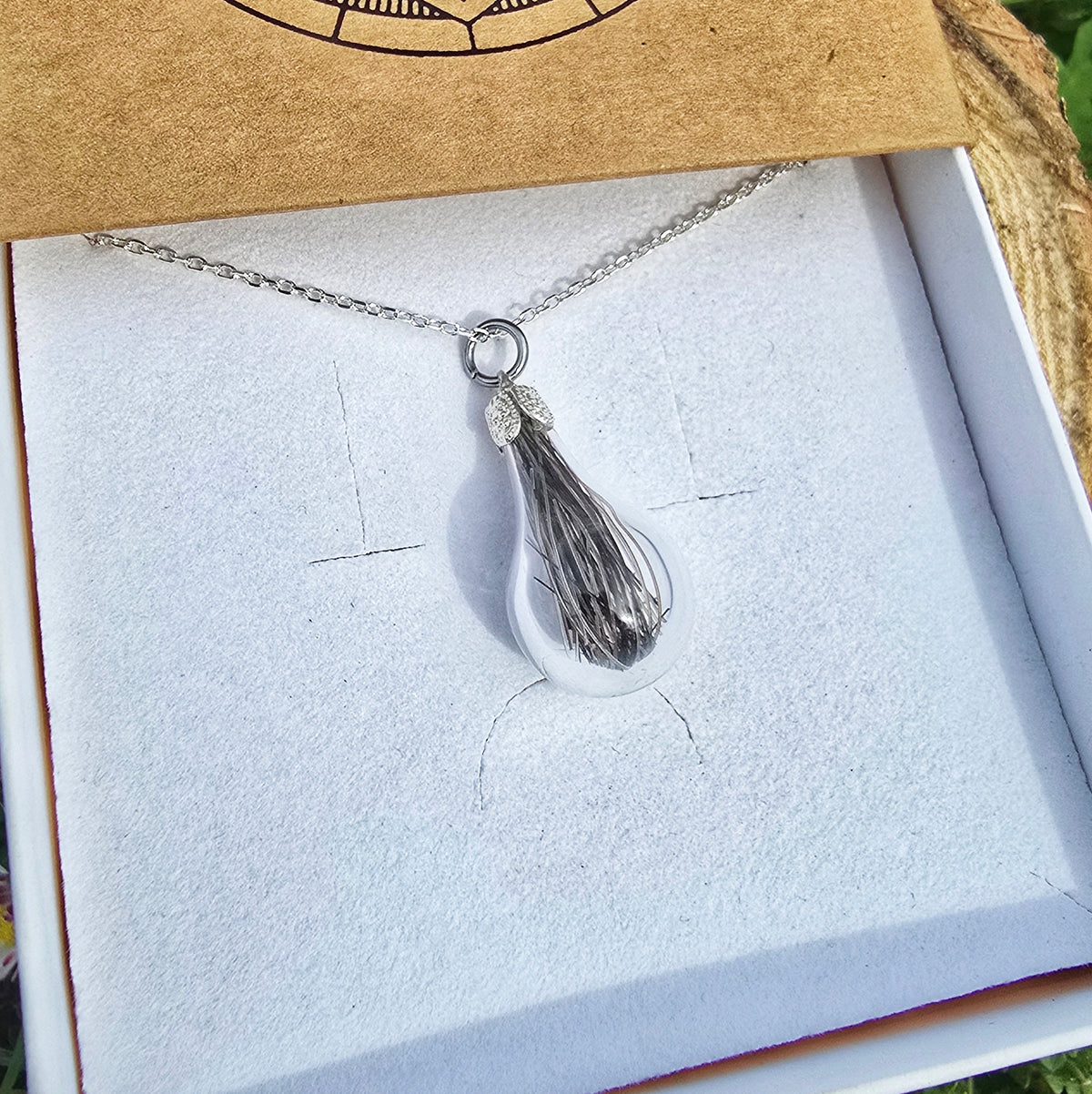 Pendentif mémorial en verre renfermant une mèche de cheveux, sur chaîne argentée, dans son écrin
